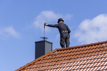 Rauchfangkehrermeister Markus Grießer reinigt einen Schornstein auf einem Hausdach unter blauem Himmel in Burgenland