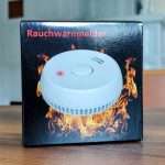 Verpackung eines Rauchwarnmelders mit Flammenhintergrund, Produktabbildung und roter Aufschrift Rauchwarnmelder