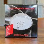 Verpackung eines Rauchwarnmelders mit Aufschrift 10-Jahres-Lithium-Batterie und VdS geprüft auf einem Holztisch
