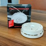 VdS-geprüfter Rauchwarnmelder mit 10-Jahres-Lithium-Batterie, geöffnet mit sichtbarer Montageplatte, vor seiner Originalverpackung