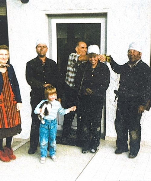 Mehrgenerationenfoto vor einem Haus mit zwei Rauchfangkehrern in Arbeitskleidung, einem Kind mit Katze und weiteren Familienmitgliedern
