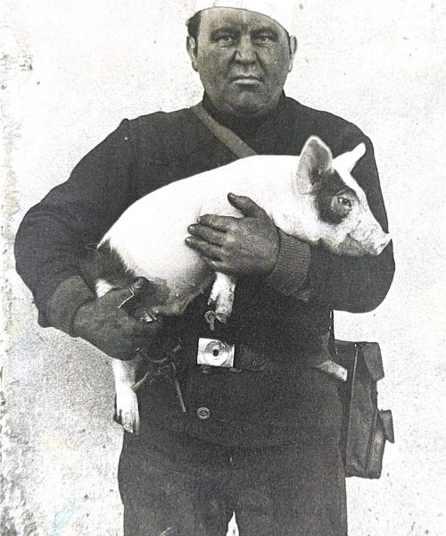 Schwarz-Weiß-Aufnahme eines Rauchfangkehrers in traditioneller Kleidung, der ein Ferkel im Arm hält – symbolträchtiges Handwerksmotiv für Glück und Tradition